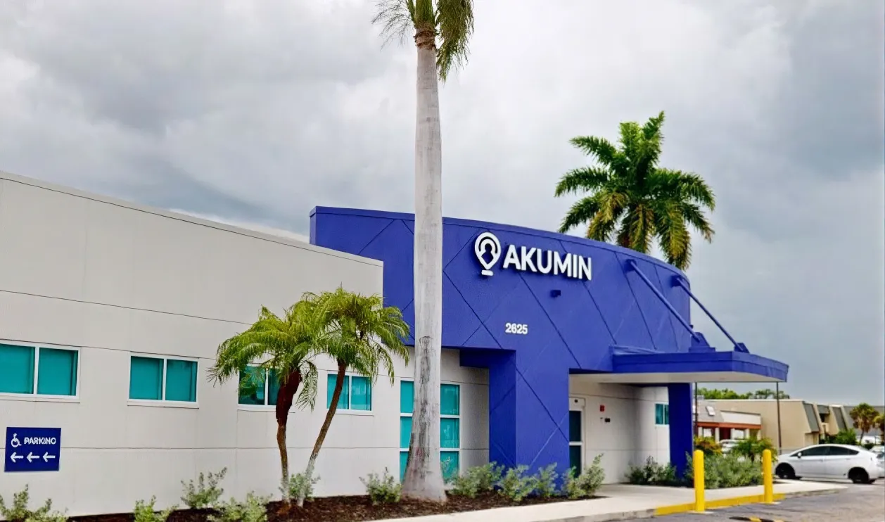 The Akumin medical imaging center, a blue and white building lined with palm trees and its parking lot