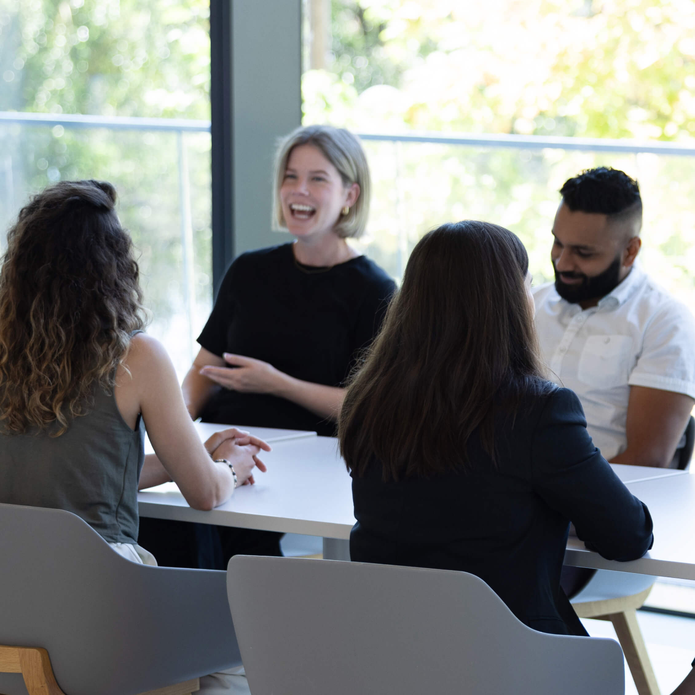 Four PocketHealth team members are seated at an office table, smiling and chatting together.