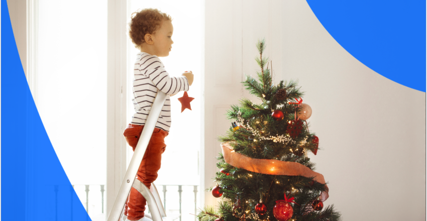 Child standing on ladder to hang ornaments on Christmas tree