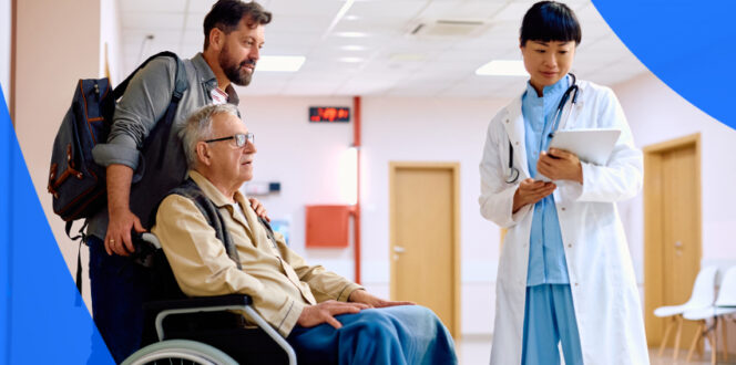Middle-age man pushes elderly man in wheelchair down hospital hallway, stopping to review medical records in Ontario with health care professional.
